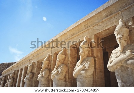 Ancient Egyptian temple facade featuring colossal statues of Hatshepsut at Luxor. Monumental stone carvings depicting the pharaoh queen in traditional regalia against clear blue sky.