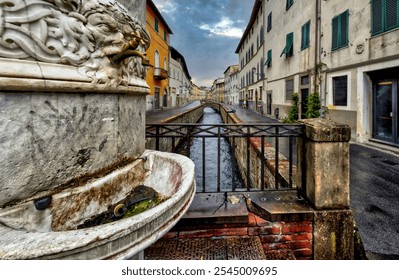 Ancient fountain, narrow canal, colorful buildings, cloudy sky, serene street scene - Powered by Shutterstock