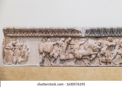 Ancient Greek Parts Of Marble Plaque With Battle Scene In Museum Of Delphi, Greece. Greek Basrelief Carved On Surface, Exhibits On White Wall Background