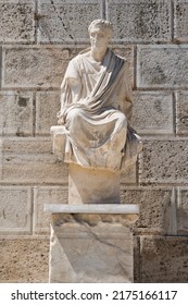 Ancient Greek Statue Below Acropolis, Athens, Greece Standing In Front Of A Big Stone Wall. Typical Historical Scene. 