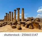 Ancient Greek Temple of Herakles ruins with Doric columns amid boulders under a blue sky in Agrigento’s Valley of the Temples, Sicily. Captures historical grandeur and natural beauty