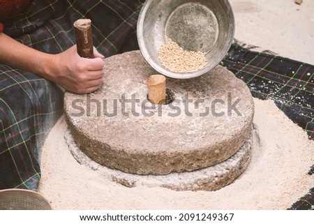 The ancient hand mill or quern stone, grinds the grain into flour. Old handmade grinding stones. The old woman is grinding flour with the traditional method.