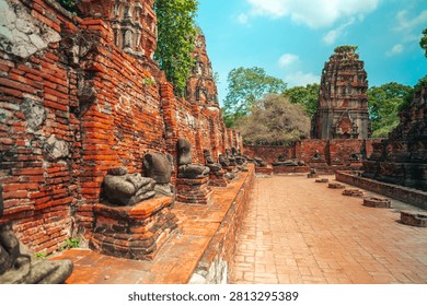 Ancient headless Buddha statues lining the red brick wall at Wat Mahathat in Ayutthaya, Thailand.