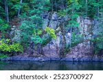 Ancient igneous rock cliffs of Interstate State Park with trees growing from the rock, along the shoreline of the St. Croix River on a summer day as seen from a riverboat cruise in Taylors Falls, MN. 