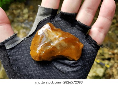 Ancient knapped flint tool held in a hand, discovered in a flowing creek, featuring glossy orange texture and primitive stone craftwork from prehistoric human history archeological find