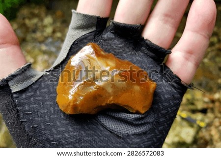 Ancient knapped flint tool held in a hand, discovered in a flowing creek, featuring glossy orange texture and primitive stone craftwork from prehistoric human history archeological find
