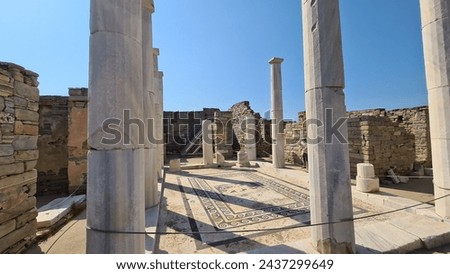 Ancient marble columns lining a paved passage among the archaeological ruins of Delos island, Greece, illuminated by strong Mediterranean sunlight.
