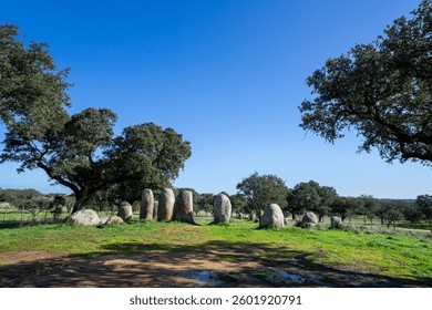Piedras megalíticas antiguas de la Cromeleque de Vale Maria do Meio en Évora, Alentejo, Portugal, de pie en un paisaje rural tranquilo bajo un cielo azul.