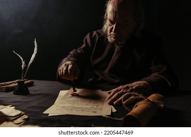 Ancient Monk Stamping Manuscript With Wax Seal Near Rolled Parchment Isolated On Black