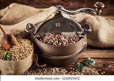 Ancient Old Cast Iron Coffee Roaster With Raw White Beans Spilling From A Rustic Hessian Sack Onto A Wooden Table