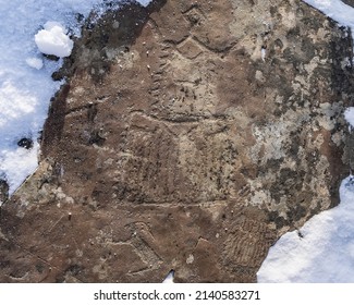 Ancient petroglyphs are carved on the stone. Mysterious drawings on a weathered surface overgrown with lichens. Snow all around. Altai. Kalbak-Tash  