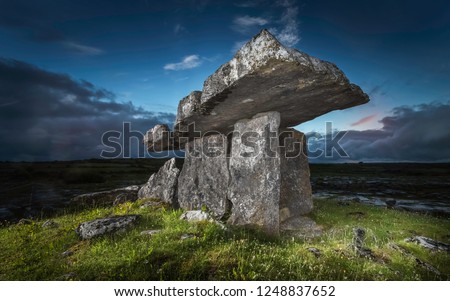 Ancient portal thomb Poulnabrone Dolmen standing on green grass in a rocky field in Glenslane Ireland lighted by flashlight before sunset with a background of blue and orange sky