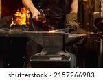 Ancient professions in the modern world. Bearded man, blacksmith manually forging the molten metal on the anvil in smithy with spark fireworks. Concept of labor, retro vintage occupation, family