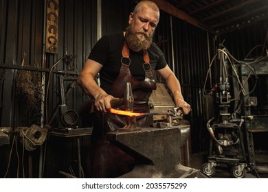 Ancient professions in the modern world. Bearded man, blacksmith manually forging the molten metal on the anvil in smithy with spark fireworks. Concept of labor, retro vintage occupation, family