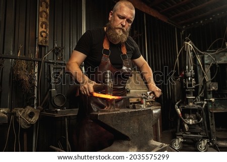 Ancient professions in the modern world. Bearded man, blacksmith manually forging the molten metal on the anvil in smithy with spark fireworks. Concept of labor, retro vintage occupation, family