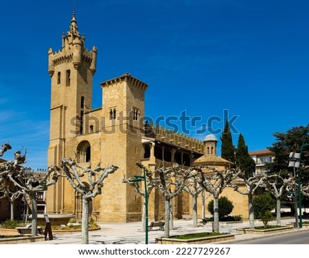 Ancient Romanesque collegiate church of Saint Savior in Ejea de los Caballeros distinguished by fortress-like appearance with crenellated bell tower against blue cloudless sky in spring, Spain