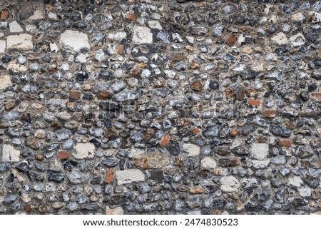 Ancient Round and Block Flint Cobblestone City Wall Stonework in Medieval England. Close-up of old building exterior with stone and mortar. Ideal Graphic Design Background or Architectural Texture.