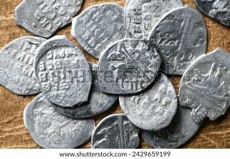 Ancient Russian coins 16th century close-up, pile of silver money of Tsar Ivan IV the Terrible. Top view of metal flakes on vintage background. Concept of old Russia, rare collection and finance.
