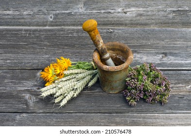 ancient rusty iron mortar and medical herbs on old wooden background. Calendula, marigold, wild marjoram, oregano and wheat ears