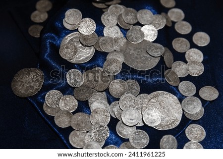 Ancient silver coins lay on deep blue silk, close up photo with selective soft focus