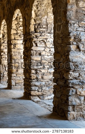 Ancient stone archway corridor with rustic masonry columns and textured rock walls, historic medieval architecture in warm natural light, timeless heritage passageway, travel destination background