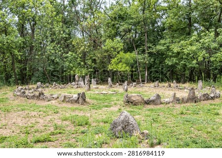 Ancient stone circle surrounded by forest trees in a natural clearing. Historic megalith arrangement with standing stones, archaeological landmark and spiritual heritage concept in peaceful woodland landscape.