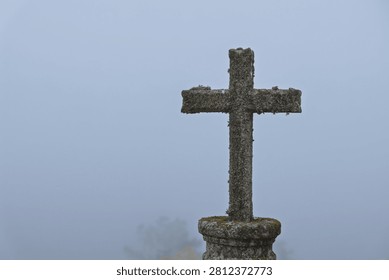 Ancient stone cross covered in moss and lichen, standing in a thick, mysterious fog