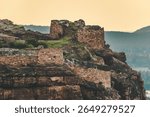 Ancient stone fort at the top of a rocky hill in Badami, Karnataka, India, illuminated by warm golden hour sunlight during sunset.