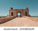 Ancient stone Mogador fort, Skala de la Kasbah, arch entrance at Essaouira coastal UNESCO landmark, the ramparts on the seafront in summer, ocean in background Morocco,