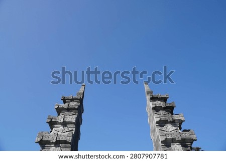 Ancient stone pillars tower under a clear, bright blue sky. Low angle shot