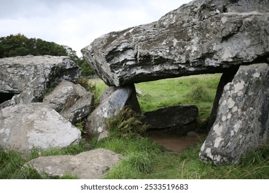 Ancient stone structure in a grassy field with trees in the background on a cloudy day. - Powered by Shutterstock