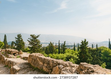 An ancient stone wall frames a cityscape nestled within hazy mountains; cypress trees punctuate the terraced landscape. A serene atmosphere evokes timeless Mediterranean beauty and hints at peaceful existence.