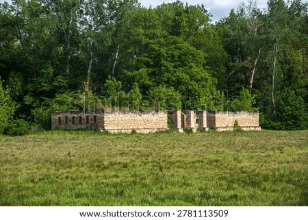 Ancient stone wall with vertical loop holes standing on grassy meadow surrounded by green trees inside historical Lednice castle park scenic landscape view