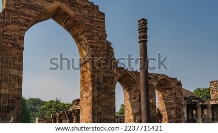 The ancient temple complex of Qutub Minar. Dilapidated arches made of red brick with carvings and ornaments on a blue sky background. The unique iron column does not rust in the foreground. India. Del