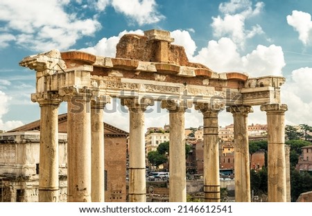 Ancient Temple of Saturn in Roman Forum, Rome, Italy, Europe. It is landmark of Rome. Old columns rise over Forum ruins and city buildings in Roma center. Concept of travel in Rome, history, culture.