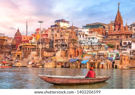 Ancient Varanasi city architecture at sunset with view of sadhu baba enjoying a boat ride on river Ganges.