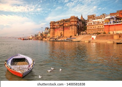 Ancient Varanasi India city architecture with view of Ganges river ghat at sunset. Wooden boat seen on river Ganga with migratory birds - Shutterstock ID 1400581838