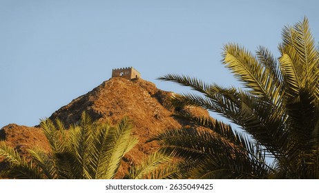 Ancient Watchtower Desert Fortress Sunset View Rugged Rocky Mountain Golden Light Vertical Framing Palm Leaves Foreground