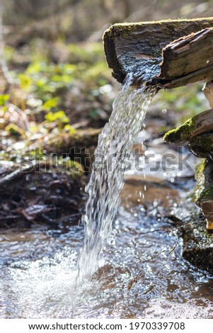 An ancient wellspring with clean drinking water in the forest. A pure, fresh, drinking water from natural source. The spring is equipped with a wooden trough for water flow