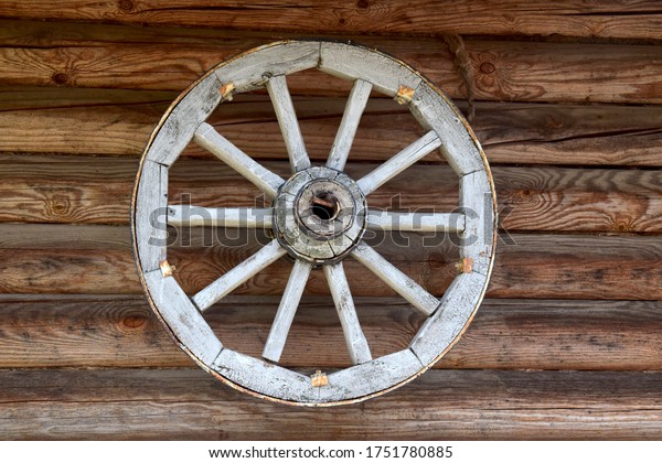 An ancient wooden wheel from the carriage\
hangs on the wall of a wooden\
house