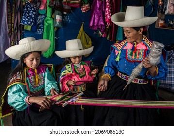 Andean Latin American mother woman making sheep's wool yarn and teaching the backstrap loom to her daughters. - Shutterstock ID 2069086130