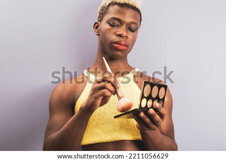 An androgynous black guy posing on a purple studio background while using cosmetics.