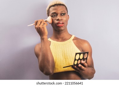 An Androgynous Black Man Posing On A Purple Studio Background While Putting On Makeup.