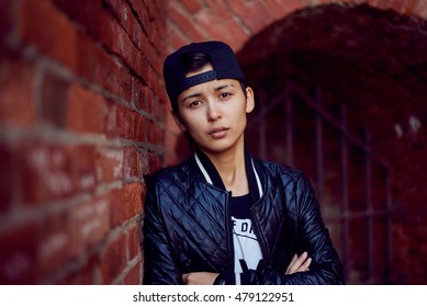 Androgynous close up portrait of asian girl in black cap and coat. Thoughtful expression emotion. Red brick wall background. - Powered by Shutterstock