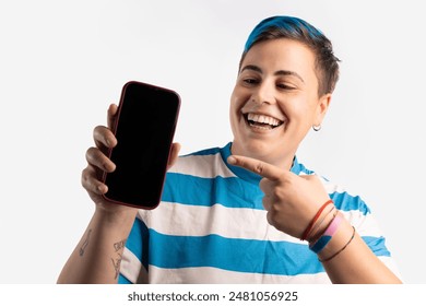 An androgynous person with blue hair, wearing a blue and white striped shirt and a pride bracelet, smiling and pointing to a smartphone screen, representing joy, technology, and LGBT pride. - Powered by Shutterstock