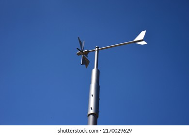 Anemometer wind speed indicator and measuring device. stainless steel tube post. wind vane, weather vane or wind cock. meteorological device. abstract low angle view. triangular blades. clear blue sky