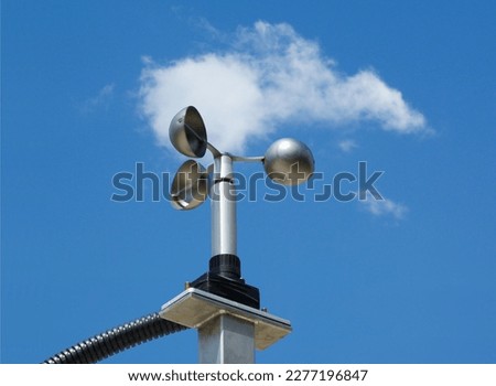 anemometer wind speed indicator measuring device fixed to aluminum bracket on tube post. meteorological device. abstract low angle view. spoon shaped semi sphere blades. blue summer sky. white clouds