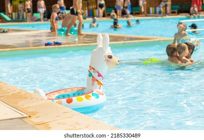 Anenii Noi,Moldova-07.01.2022:llama Inflatable Ring Swimming Balloon Floats On Water Pool.lot Of Childrens Are Playing In The Background,enjoy The Summer Time,heat Warm Weather.cute Llama Shape