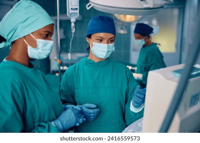 Anesthesiologist communicating with African American female surgeon about patient's vitals on the screen during surgery in the hospital. - Powered by Shutterstock