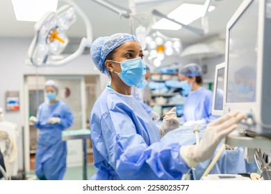 Anesthetist Working In Operating Theatre Wearing Protecive Gear checking monitors while sedating patient before surgical procedure in hospital - Powered by Shutterstock